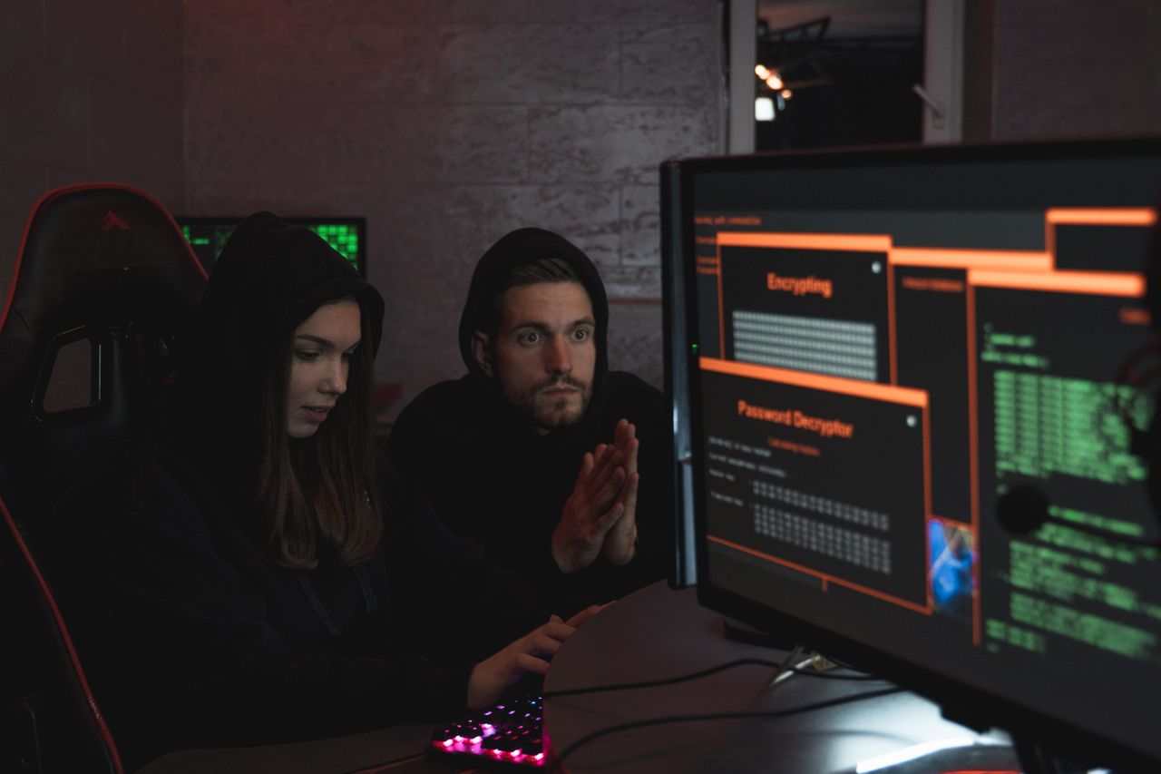 Home Cybersecurity experts in hoodies analyzing encrypted data on computer screens in an indoor setting.